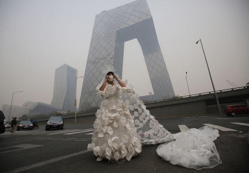 Kong Ning wears a wedding dress decorated with 999 face masks for her performance art work 'Marry the blue sky' as she poses for a photograph in front of the China Central Television (CCTV) Headquarters on a hazy day in Beijing November 19, 2014. Wearing a 10 meter-long wedding dress decorated with face masks is a part of Kong Ning's performance art work which signifies her frustration with air pollution. REUTERS/Kim Kyung-Hoon