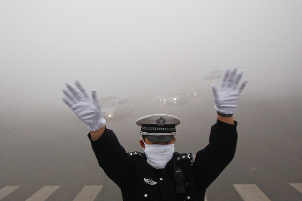 A traffic policeman signals to drivers during a smoggy day in Harbin, Heilongjiang province, October 21, 2013. The second day of heavy smog with a PM 2.5 index has forced the closure of schools and highways, exceeding 500 micrograms per cubic meter on Monday morning in downtown Harbin, according to Xinhua News Agency. REUTERS/China Daily (CHINA - Tags: ENVIRONMENT TRANSPORT) CHINA OUT. NO COMMERCIAL OR EDITORIAL SALES IN CHINA - RTX14IFX