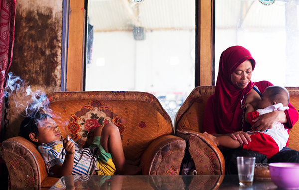 Dihan Muhamad, who used to smoke up to two packs of cigarettes a day before cutting down, poses for a photo as he smokes while his mother breast feeds his younger brother at their home in the village near the town of Garut, Indonesia on February 10, 2014.
