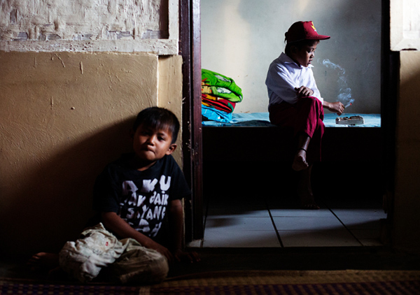 Ilham Hadi, who has smoked up to packs a day and began when he was four years old, poses for a photo wearing his third grade uniform while smoking in his bedroom as his younger brother looks on in their village near the town of Sukabumi, Indonesia on February 14, 2014.