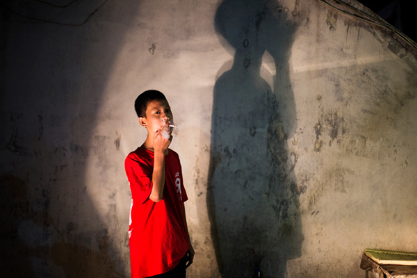 Andika Prasetyo, who smokes about a pack a day, has a cigarette outside an internet cafe where children are smoking inside in Depok, West Java, Indonesia on February 15, 2014.